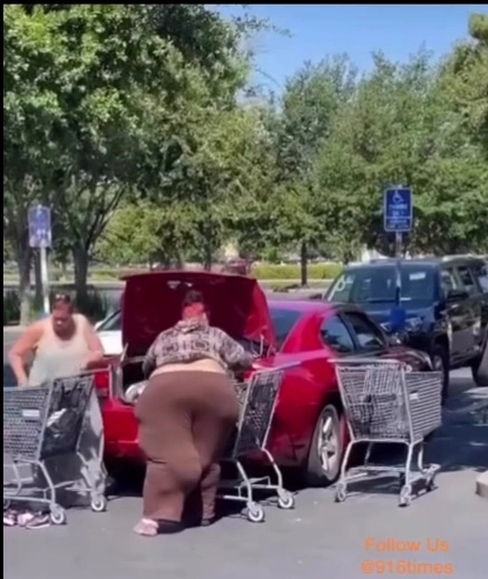 large woman in brown pants loading items into trunk of red car